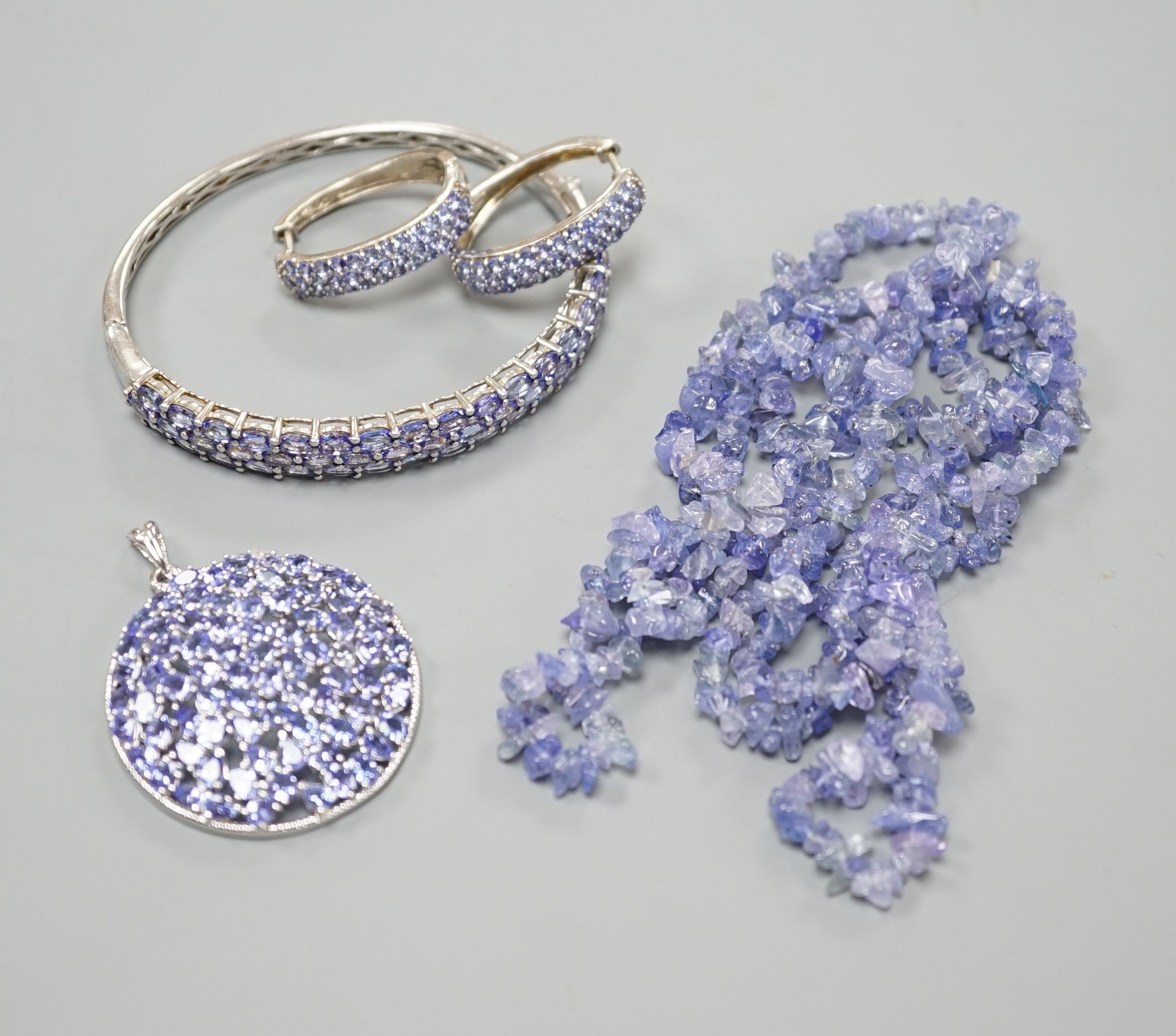A modern 925 and tanzanite set hinged bangle, a similar pair of earrings and pendant and a rough cut tanzanite set necklace.